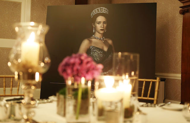 Dinner table with candle light and fuchia flower and poster of Queen Elizabeth as in The Crown series in the background 