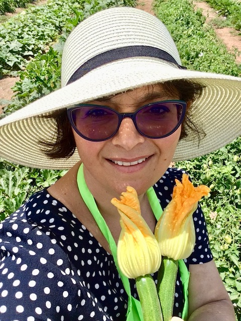 woman wearing blue spectacles and white hat posing with courgette zucchini flowers for mums magazine