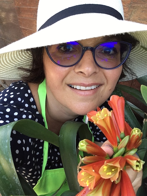 woman wearing blue spectacles and white hat posing with orange flowers for mums magazine