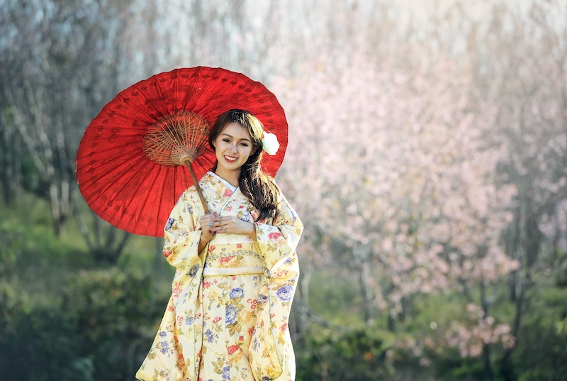 young woman wearing a yellow kimono and holding red parasole umbrella posing for mums magazine