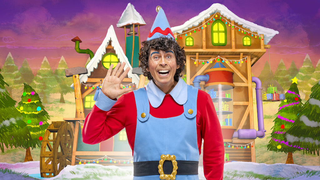 Andy Day wearing elf costume waving hallo with candy floss house in the background posing for mums magazine 