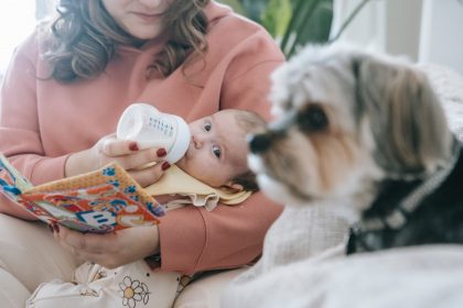 mum feeding baby with baby formula while child watches puppy dog posing for mums magazine