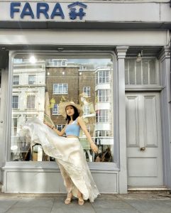 Woman stood outside FARA charity shop in Kensington London with floaty skirt blowing in breeze