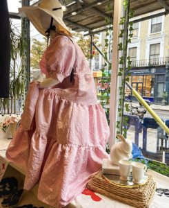 mannequin seated in shop window wearing hat and long pink dress