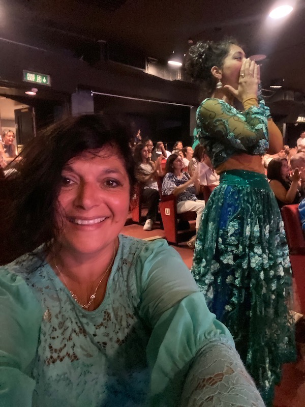 woman wearing emerald green top posing for mums magazine near Indian dancer on stage of west end show beyond bollywood