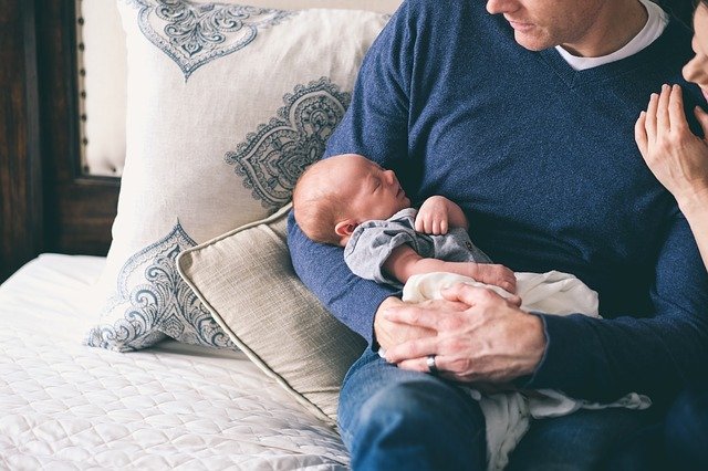 father wearing a blue jumper holding a baby in his arms posing for mums magazine 