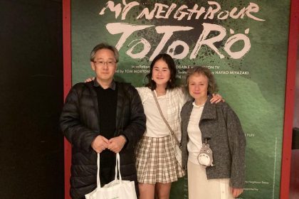 family posing for mums magazine in front of Totoro poster for Barbican theatre show