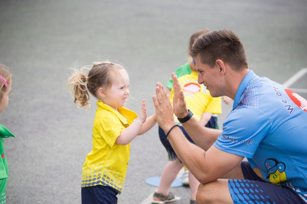 toddler girl wearing a yellow shirt plays with sport teacher 