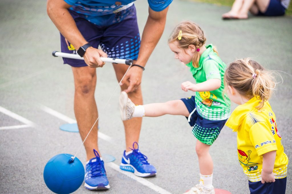 school girls wearing a yellow and green shirt play with sport teacher 