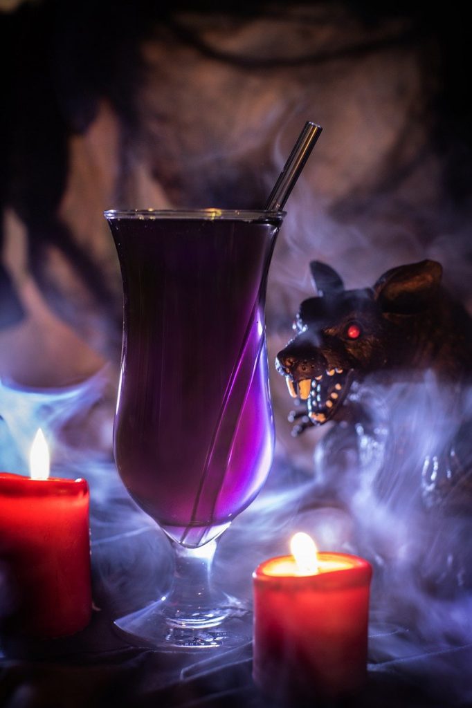 The Witches Cocktail in purple juice surrounded by candles 