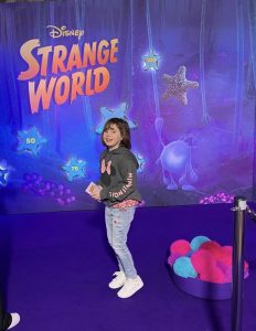 child posing for mums magazine in front of disney strange world poster 