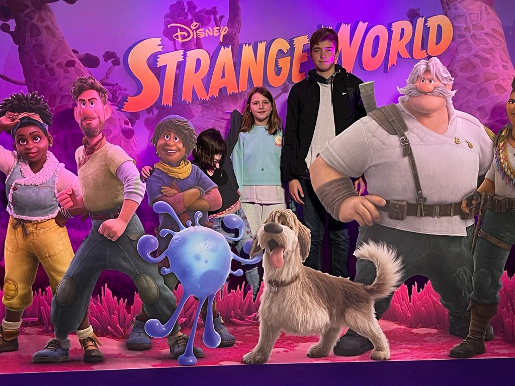 group of children posing for mums magazine in front of disney strange world movie poster