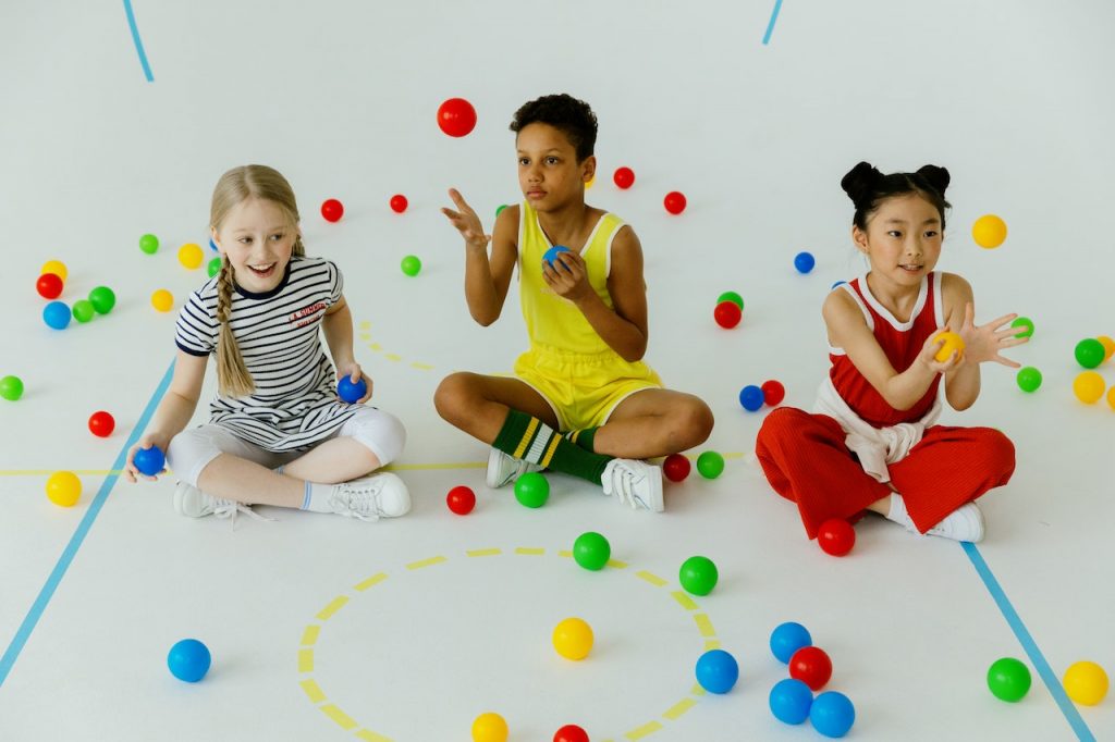 three children sitting on the floor catching colourful balls posing for mums magazine 