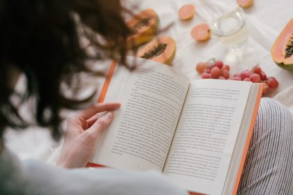 woman reading a book while eating papaya and grapes