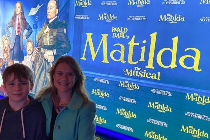 Mother and teenage son attending Matilda the musical multimedia screening in london posing in front of movie poster for mums magazine