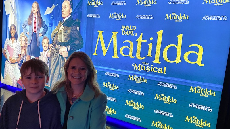 Mother and teenage son attending Matilda the musical multimedia screening in london posing in front of movie poster for mums magazine 