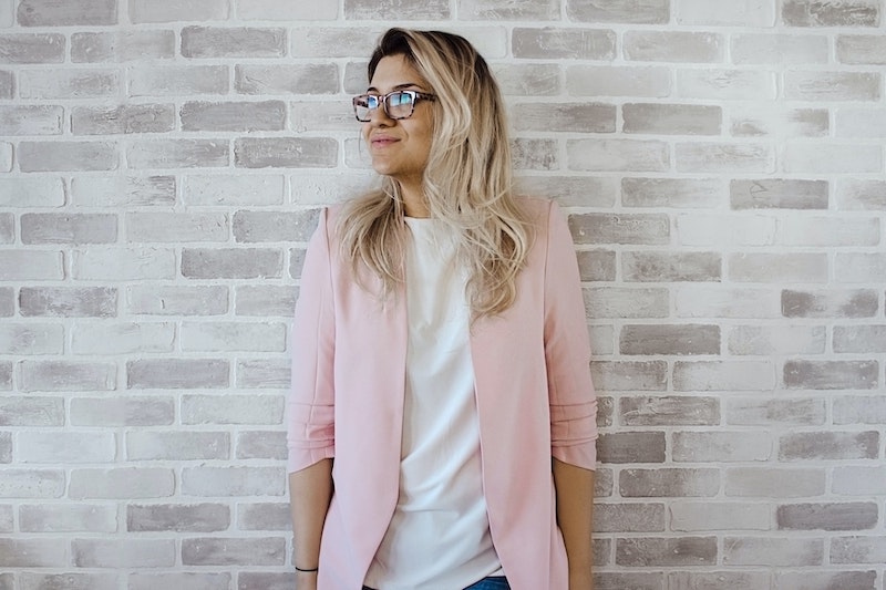 woman standing against a brick wall wearing a pink cardigan posing for mums magazine