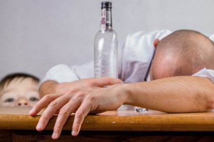 man lies on table drunk being watched by young child
