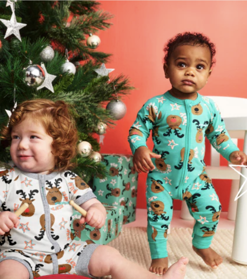 toddlers wearing colourful jumpsuits playing near the christmas tree 
