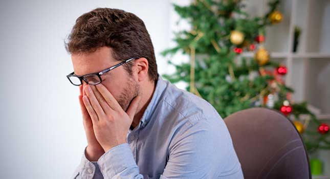 man looking desperate sitting next to the Christmas tree
