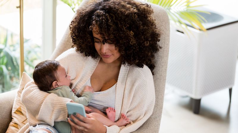 mum holding a baby on the couch while browsing 